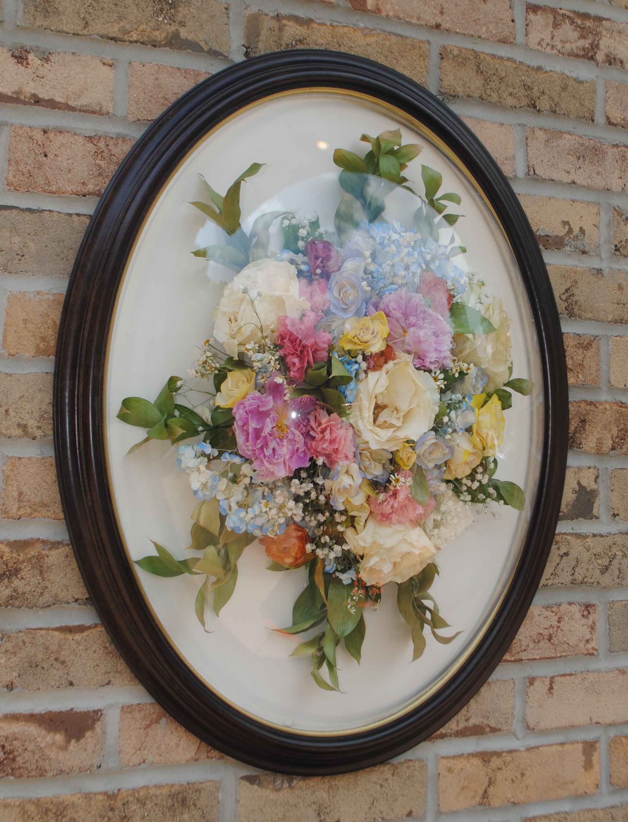 Dimensional dome flower preservation with colorful preserved flowers in black oval frame